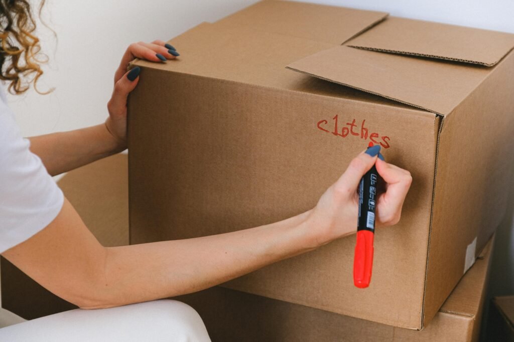 pexels-photo-7203971-7203971 Close-up of a woman labeling a cardboard box with a red marker indoors.